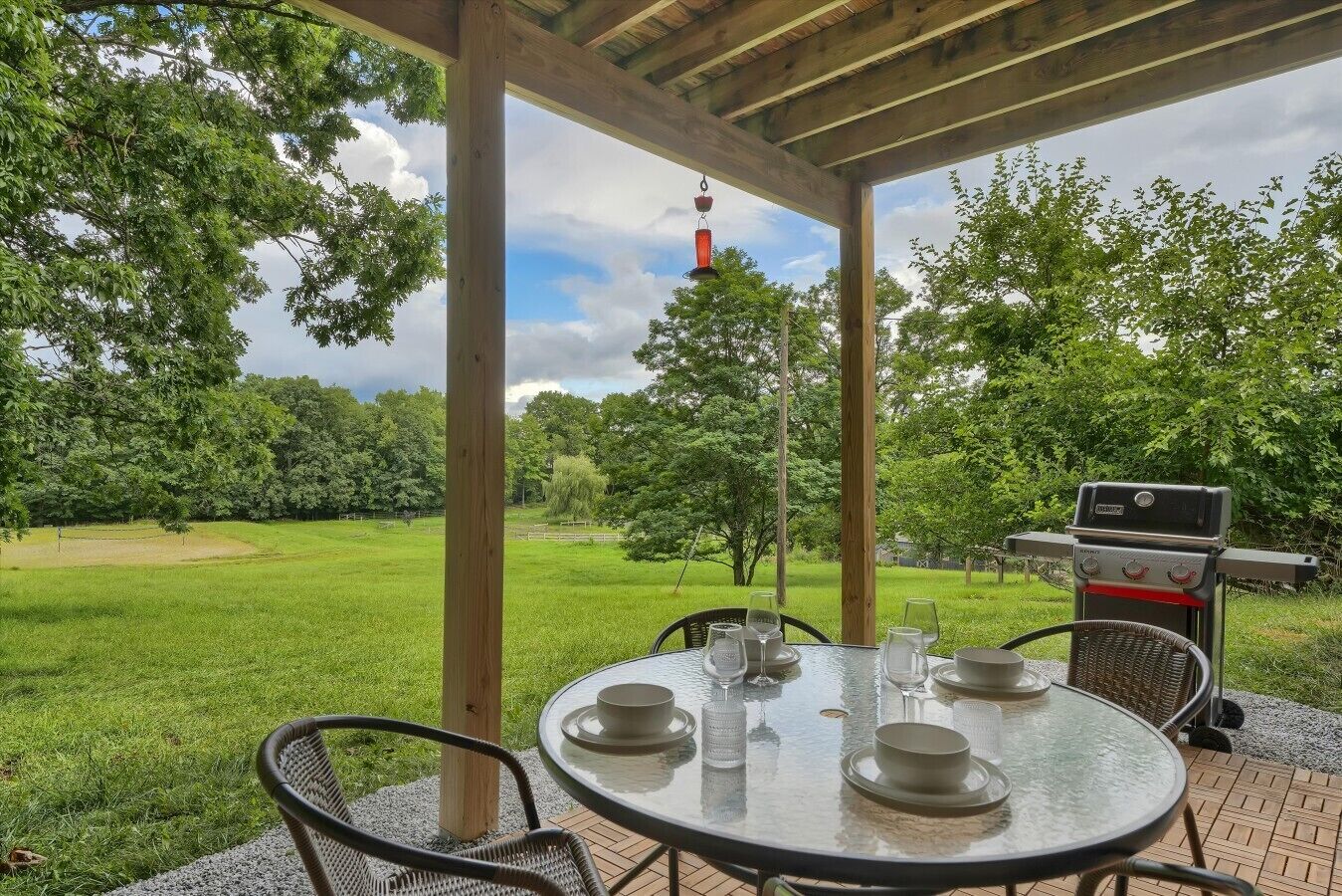 Une terrasse extérieure avec une table ronde dressée pour le repas, entourée de chaises, et un barbecue en arrière-plan.