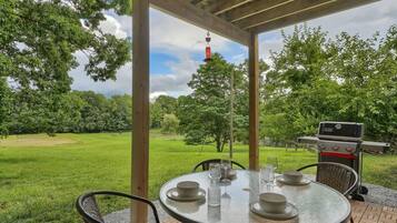 Une terrasse extérieure avec une table ronde dressée pour le repas, entourée de chaises, et un barbecue en arrière-plan.