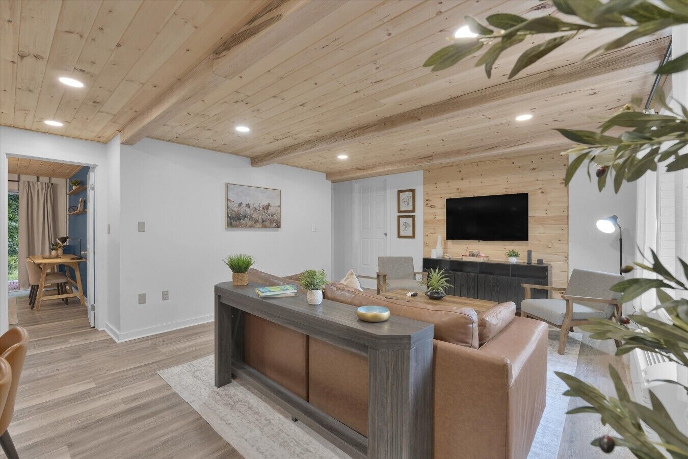 A modern living room with a wooden ceiling, a large TV, a sofa, and a dining area.