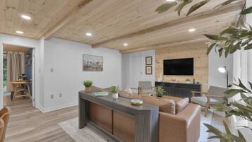 A modern living room with a wooden ceiling, a large TV, a sofa, and a dining area.