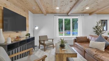 Una sala de estar moderna con techo de madera, un televisor de pantalla plana, un sofá, una mesa de centro y una silla.