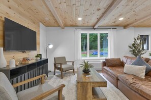 Ein modernes Wohnzimmer mit Holzboden, einem Flachbildfernseher, einer Couch, einem Couchtisch und einem Sessel.