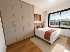 A bedroom with a bed, a wardrobe, a window with a city view, and a painting on the wall. - Chanes Street (São Paulo)