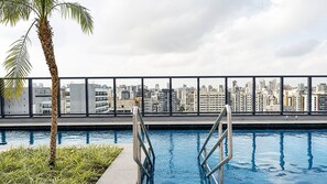 A rooftop pool with a city skyline view, metal poolside railings, and a palm tree. - Chanes Street (São Paulo)