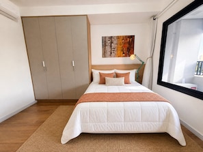 A bedroom with a bed, a wardrobe, a painting, a lamp, and a window. - Chanes Street (São Paulo)