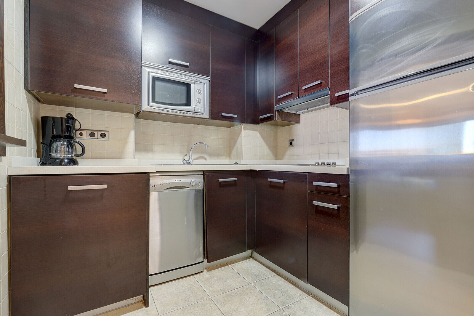 A modern kitchen with dark wooden cabinets, a stainless steel dishwasher, a microwave, and a refrigerator.