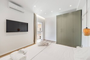 A modern bedroom with a bed, a TV mounted on the wall, a wardrobe, and a window with curtains. - Aqua Breeze Golem 2BR Apartment (Golem)