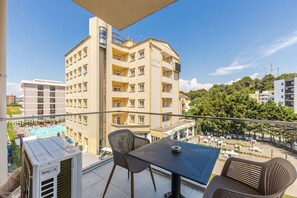A balcony with a table and chairs, overlooking a swimming pool and a hotel building. - Aqua Breeze Golem 2BR Apartment (Golem)