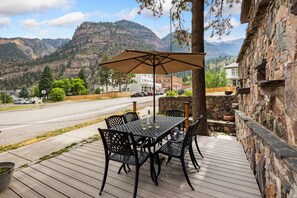 Une terrasse extérieure avec une table et des chaises, un grand parasol et une vue sur les montagnes et une rue.