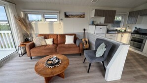 A modern living room with a brown sofa, a grey armchair, and a wooden coffee table. - Camping Zeezicht - Chalet 16 (Westerland)