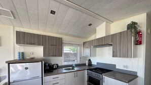 A modern kitchen with wooden cabinets, a built-in oven, a refrigerator, and a window. - Camping Zeezicht - Chalet 16 (Westerland)