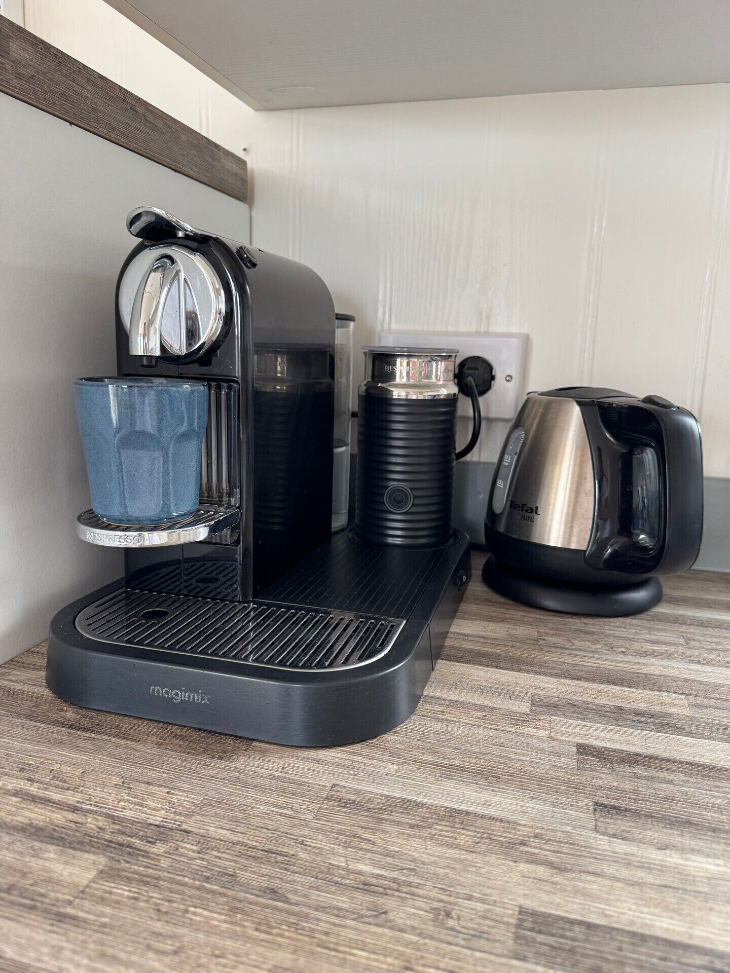 En kaffemaskin med ett vattenreservoir, en kaffekanna och en vattenkokare placerade på en träyta.