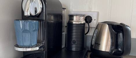 En kaffemaskin med ett vattenreservoir, en kaffekanna och en vattenkokare placerade på en träyta.