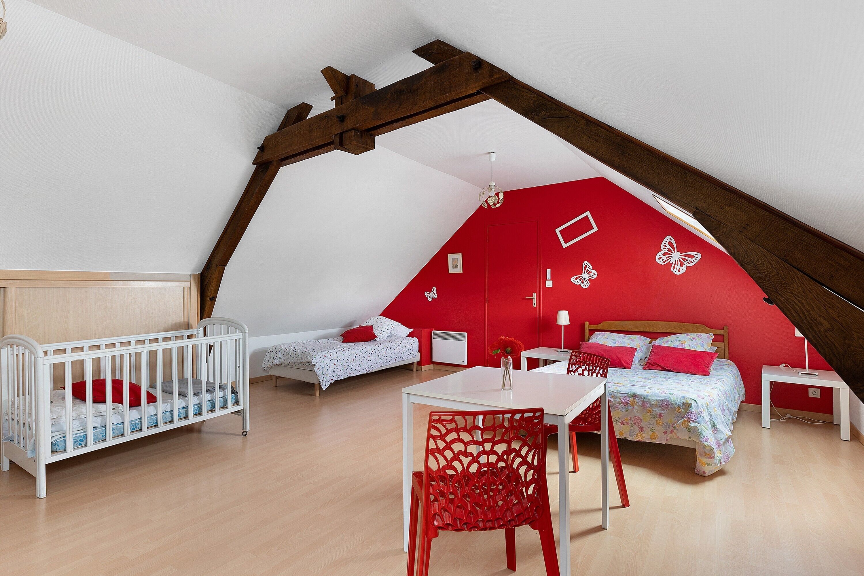 Ein Zimmer mit geneigter Decke, einem Kinderbett, einem Bett, einem Esstisch und einem Stuhl.