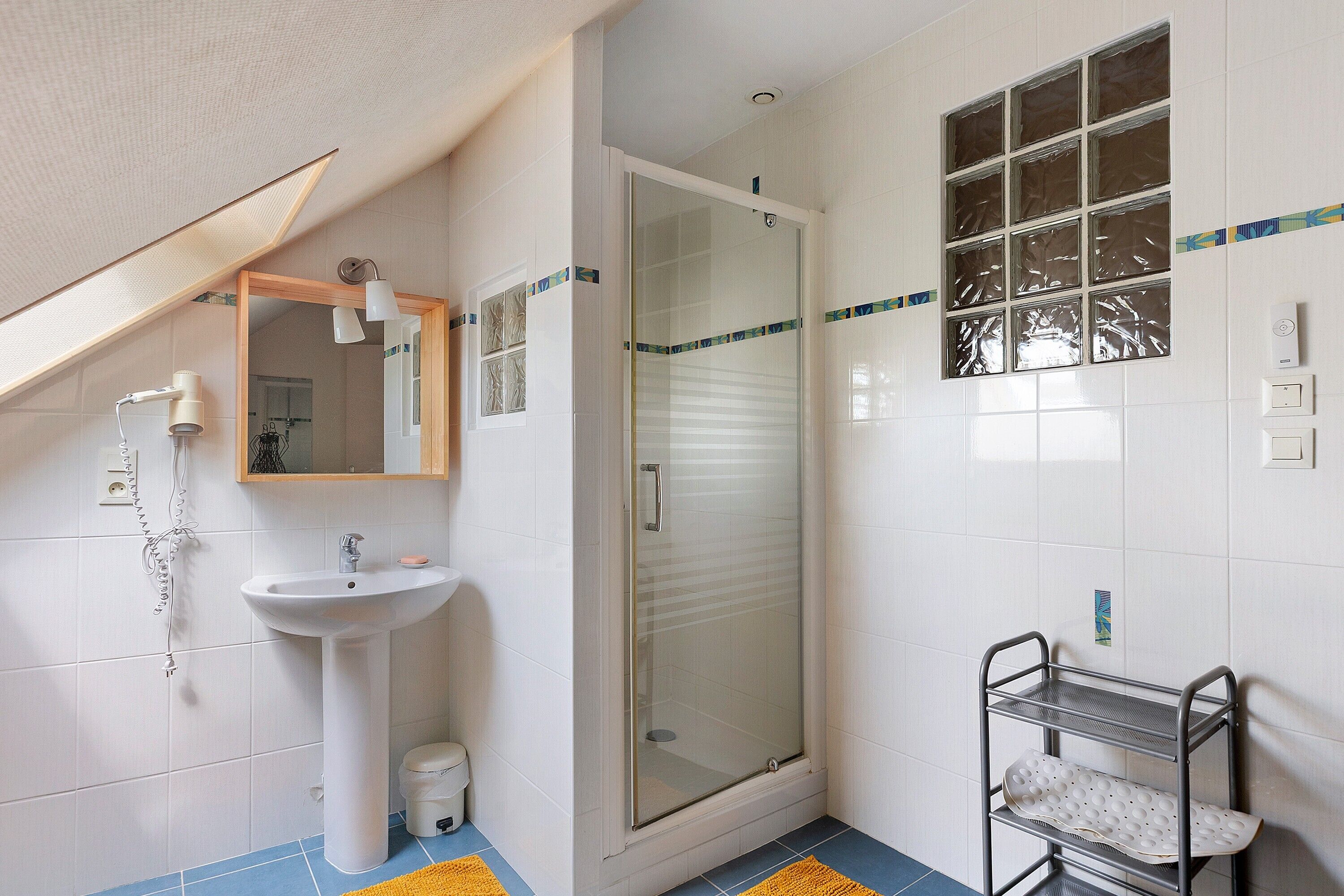 Ein Badezimmer mit einem Standwaschbecken, einer Duschkabine, einem Spiegel und einem Metallregal.