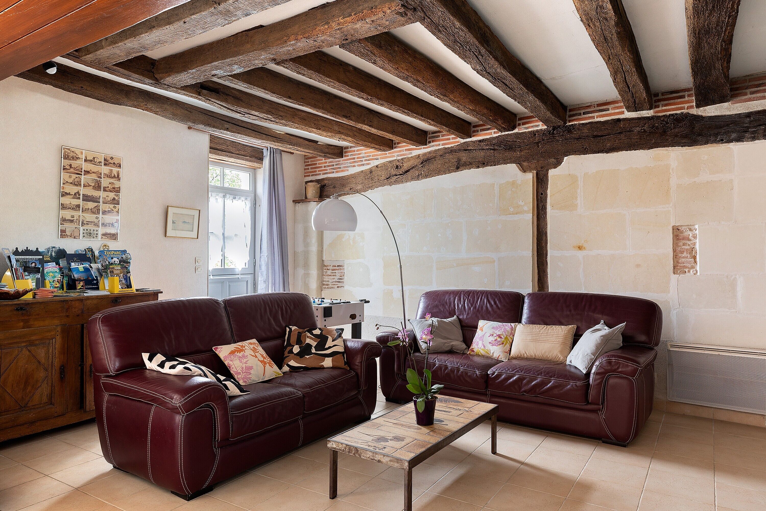 Ein Wohnzimmer mit zwei Ledersofas, einem Holztisch und sichtbaren Holzbalken an der Decke.