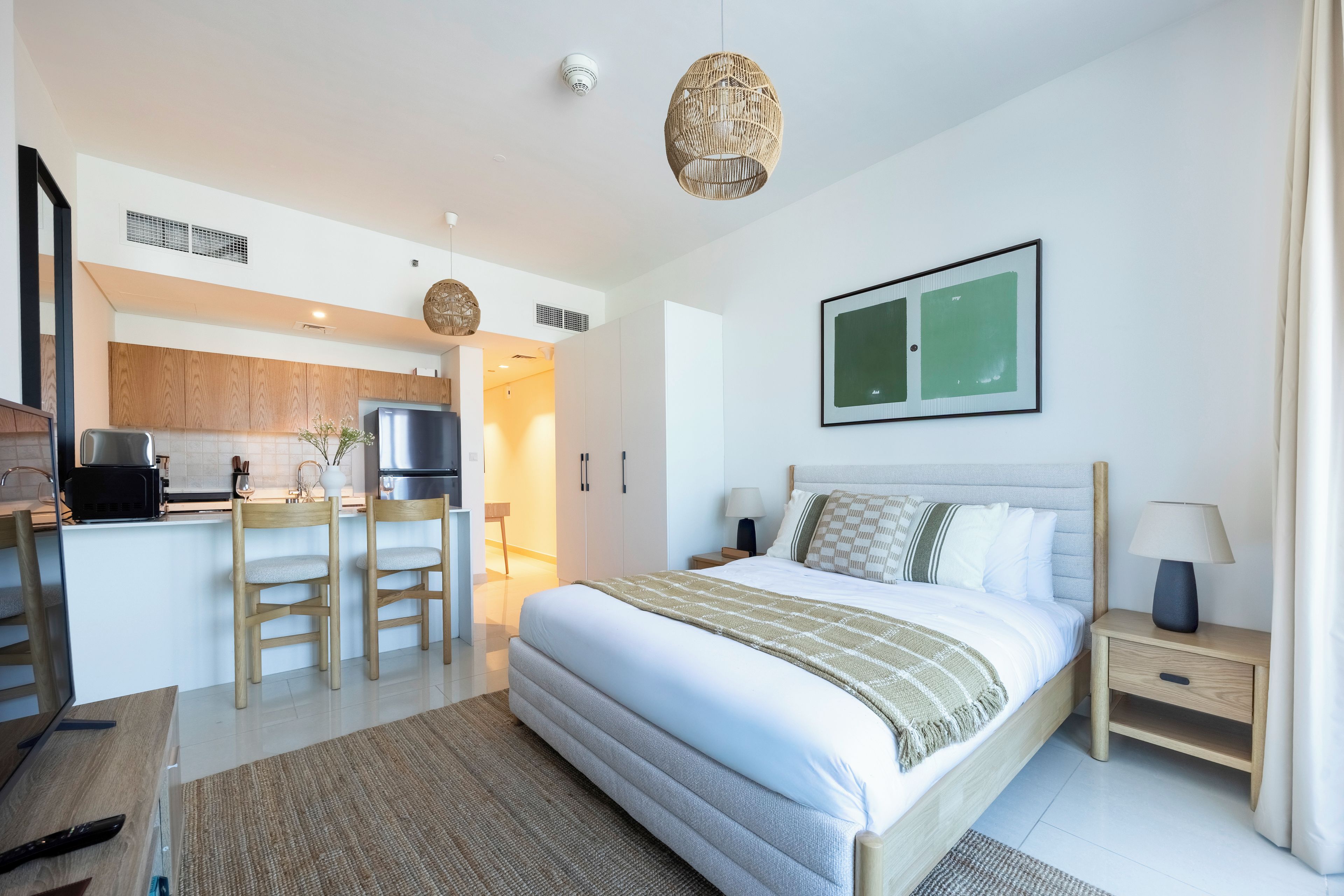 A modern hotel room with a bed, bedside table, and a view of the kitchen area.