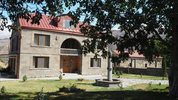 A stone building with a red roof, a central entrance with a wooden door, and a small garden area with a fountain.
