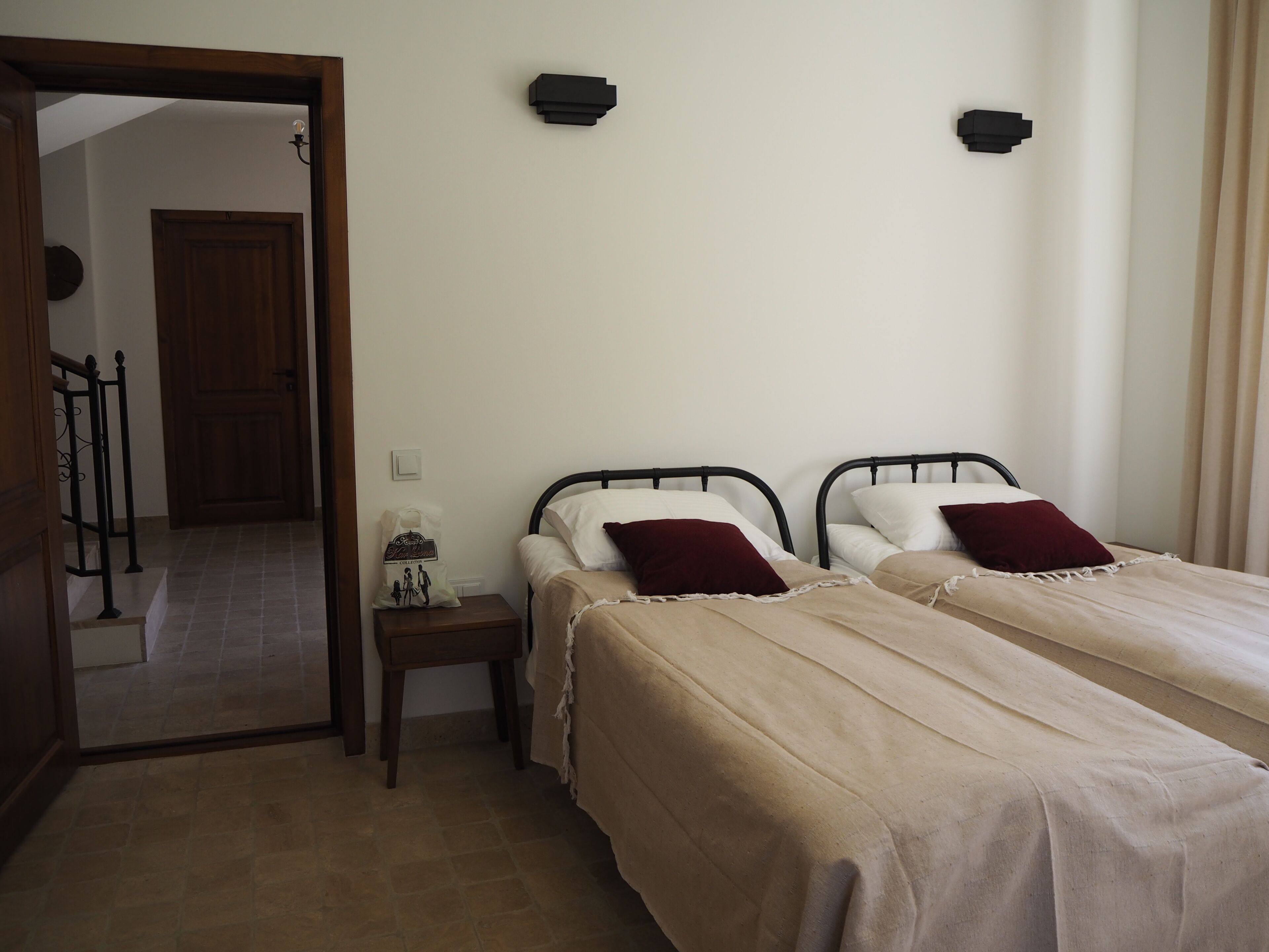 A bedroom with two beds, a nightstand, a wooden door, and a light switch on the wall.