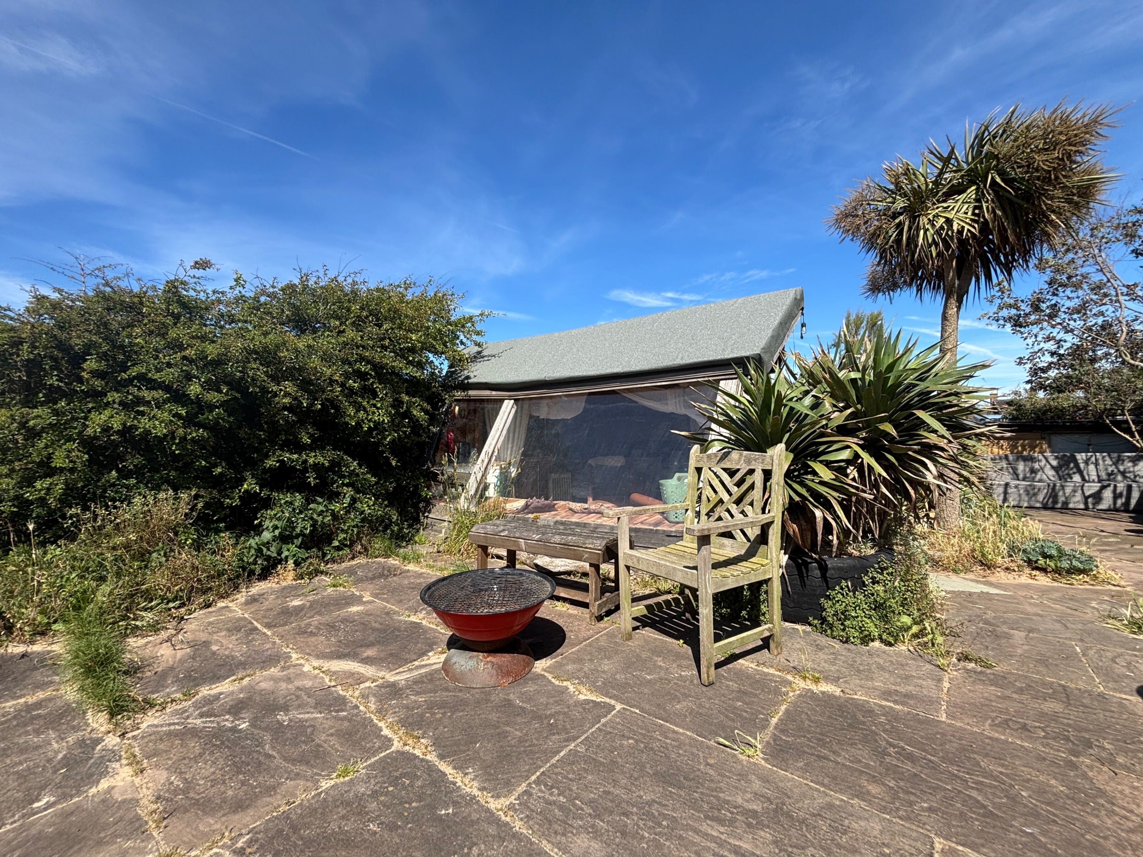 Un espace extérieur aménagé avec des meubles de jardin, comprenant une table et des chaises, protégé par un auvent et entouré de dalles de pierre et de verdure.
