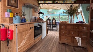 A rustic kitchen with wooden cabinets, a stove, a sink, and a dining area with chairs. - Private Cosy Cabin With sea View Sleeps 2 (Liverpool)