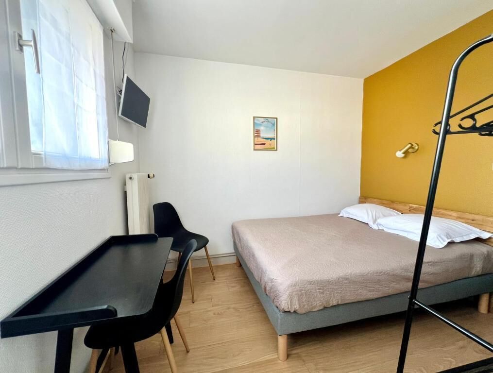 A bedroom with a bed, a desk, a chair, a TV, and a wall-mounted shelf.