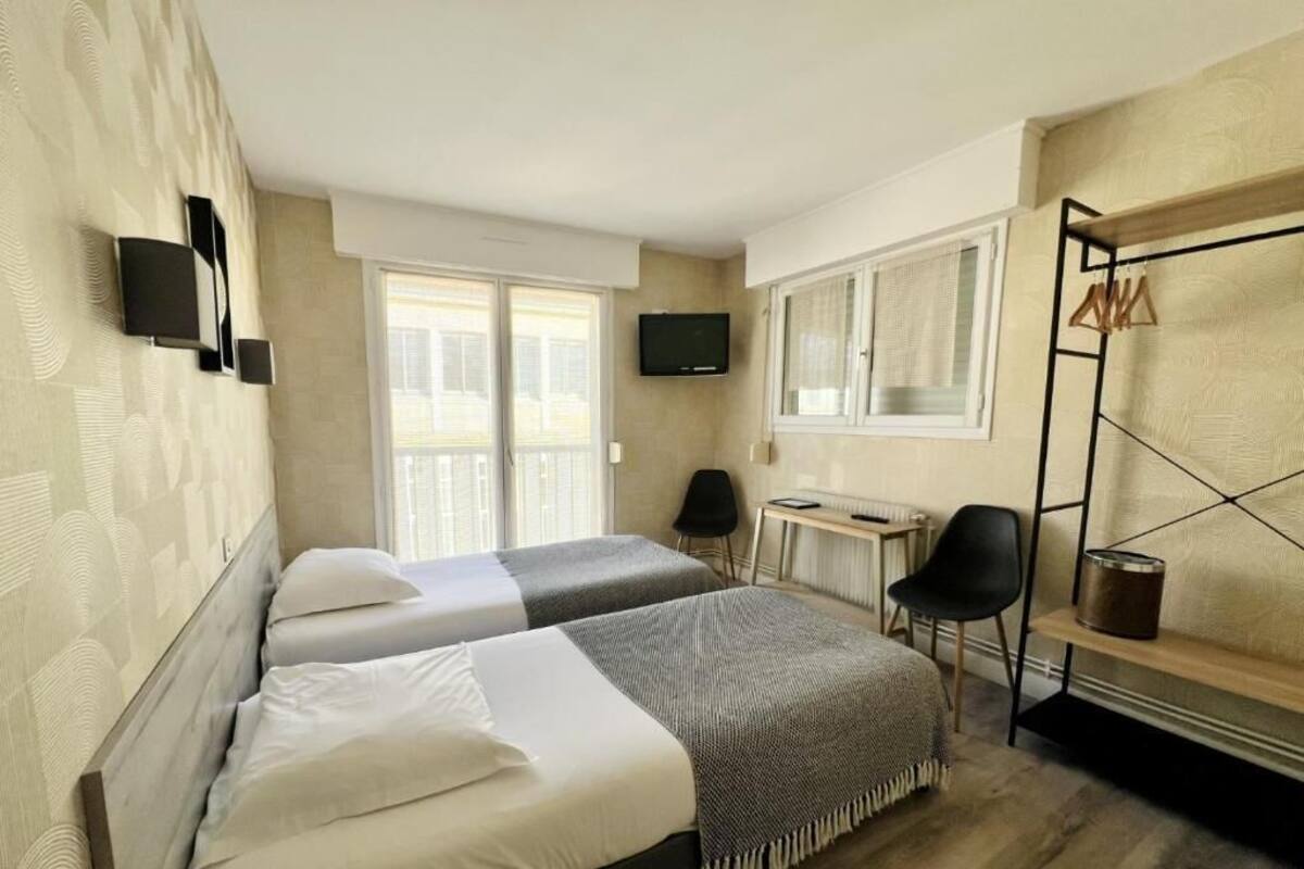 Une chambre d’hôtel avec deux lits, une télévision, un bureau et une fenêtre avec des rideaux.