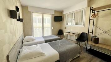 Habitación de hotel con dos camas, televisor, escritorio y ventana con cortinas.