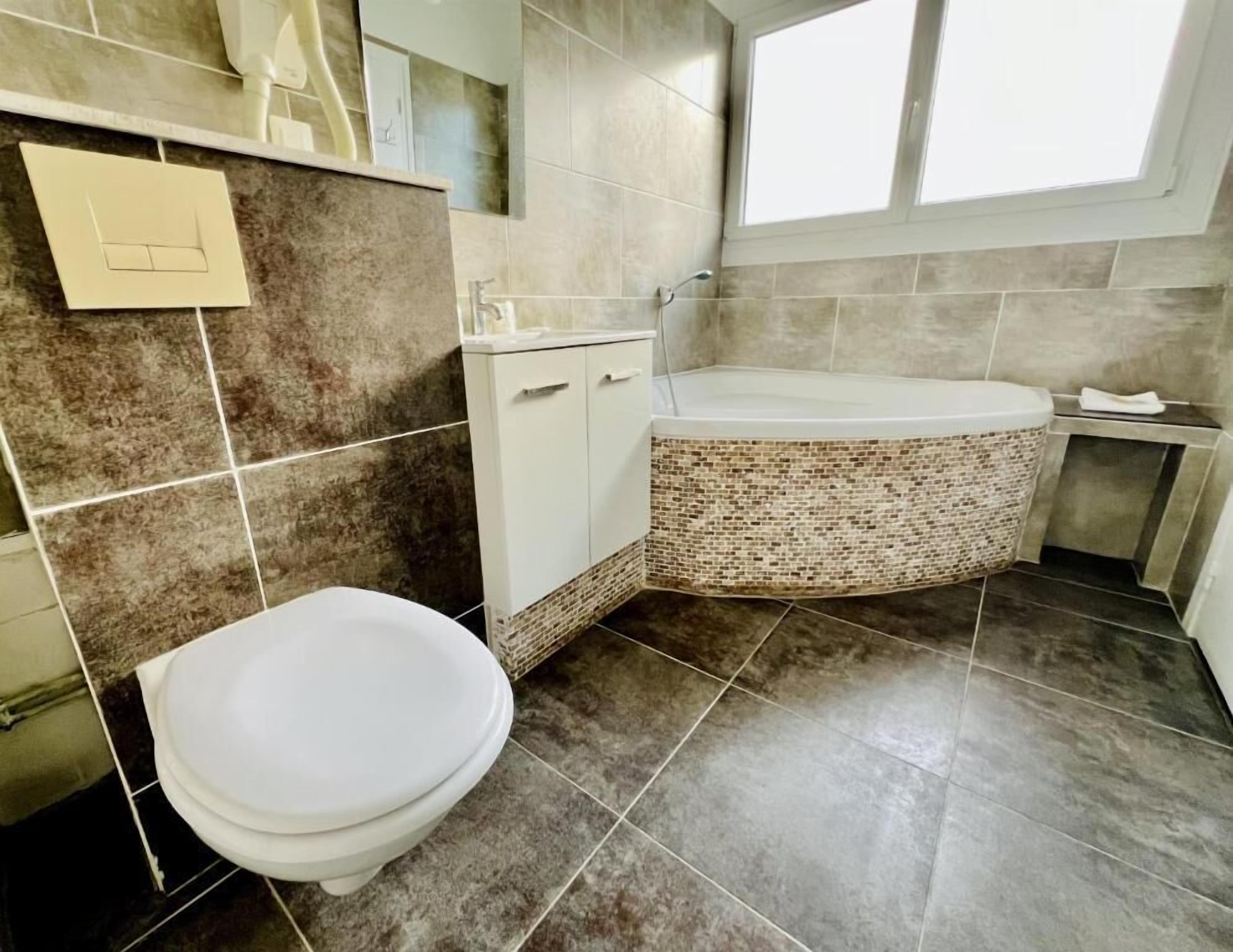 A bathroom with a toilet, a sink, a mirror, and a bathtub with a mosaic tile surround.