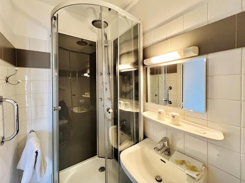 Une salle de bain moderne avec une douche en verre, un lavabo blanc et un miroir au-dessus du lavabo.