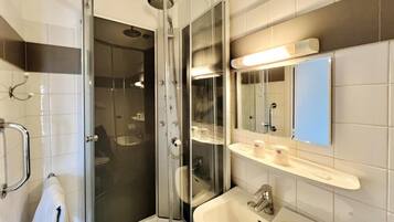 Une salle de bain moderne avec une douche en verre, un lavabo blanc et un miroir au-dessus du lavabo.