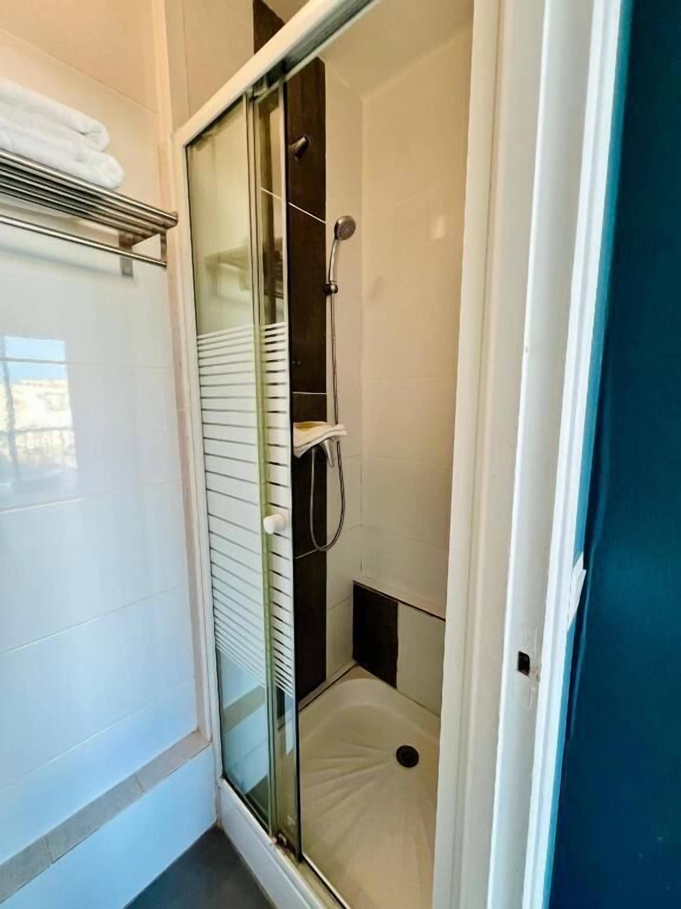 A glass-enclosed shower stall with a white tiled floor, a glass door, and a towel rack above it.