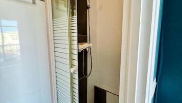 A glass-enclosed shower stall with a white tiled floor, a glass door, and a towel rack above it.