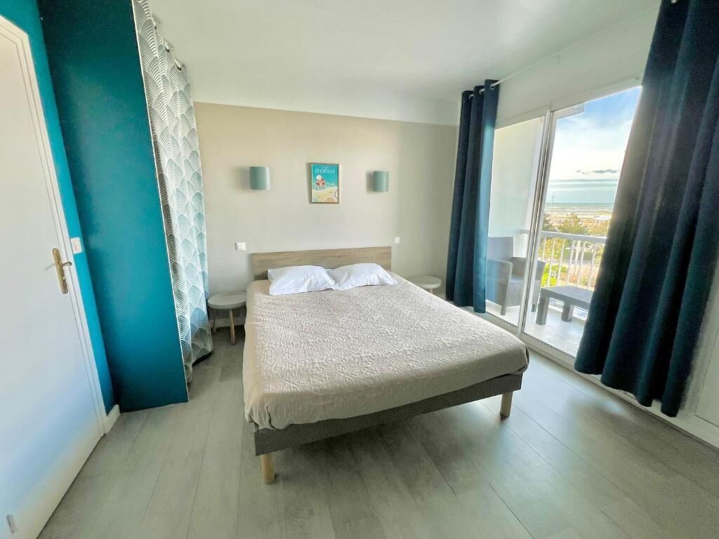 Ein Hotelzimmer mit einem Bett, einem kleinen Tisch, einem Stuhl, einem Fenster mit Vorhängen und Blick nach draußen.