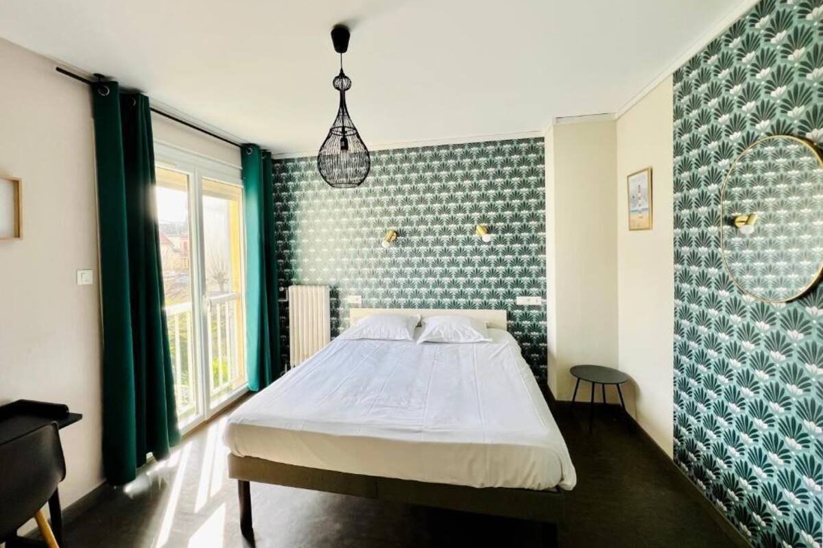 Une chambre à coucher avec un lit, une chaise, un bureau, une fenêtre avec des rideaux et un papier peint à motifs.