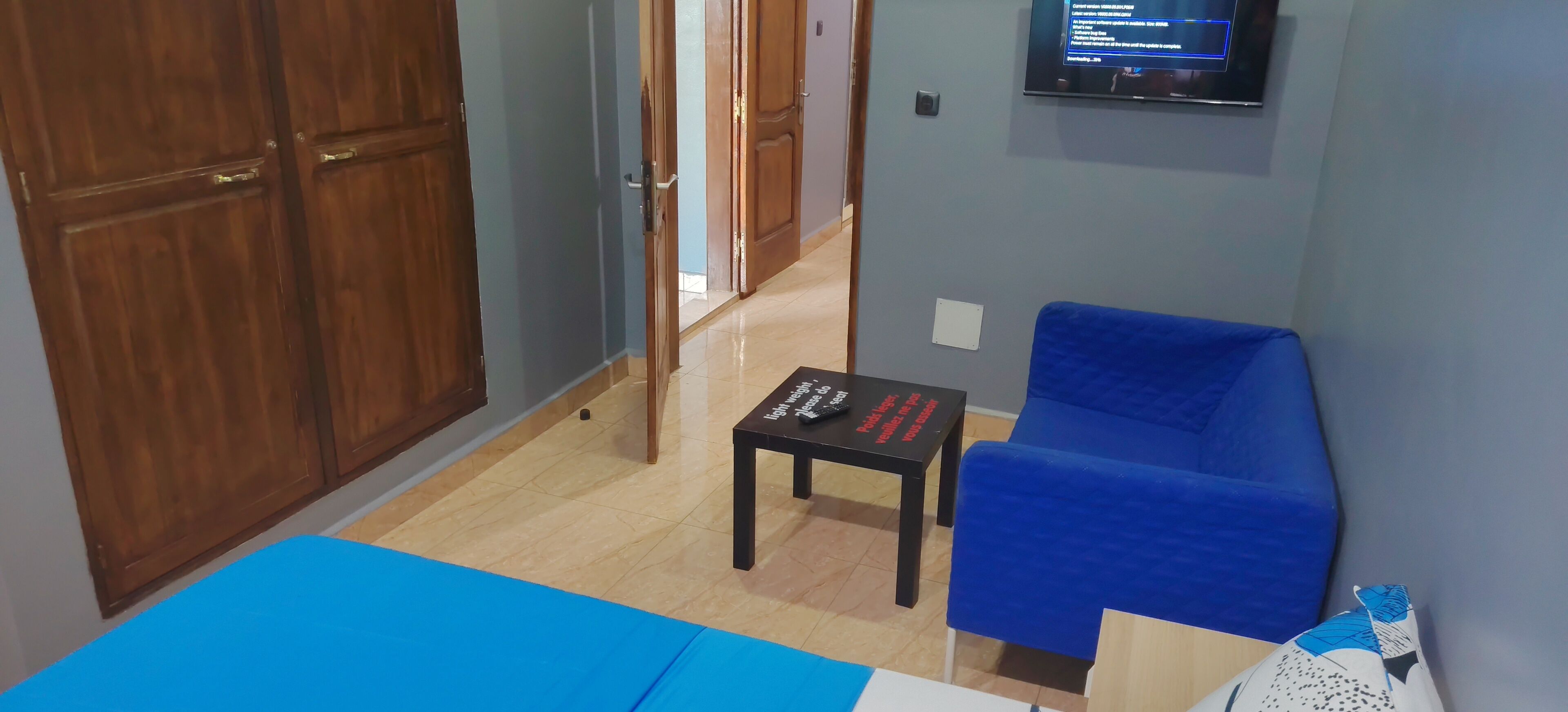 Une pièce avec un canapé bleu, une petite table sur laquelle se trouve une télécommande et un téléviseur fixé au mur.