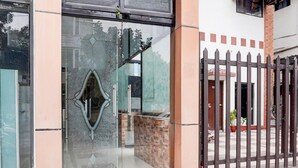 Una entrada de edificio con puerta de vidrio, portón metálico y un camino de baldosas que lleva a la entrada.