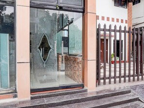A building entrance with a glass door, a metal gate, and a tiled pathway leading to the entrance. - Deluxe Hotel Shivam Residency (Dehradun)