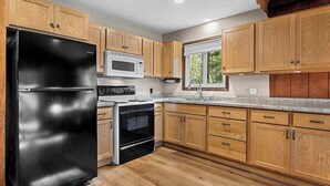 Une cuisine avec des meubles en bois, un réfrigérateur noir, un four à micro-ondes et une cuisinière.
