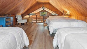 Une chambre mansardée avec des lambris en bois, un lit, une chaise et une commode.