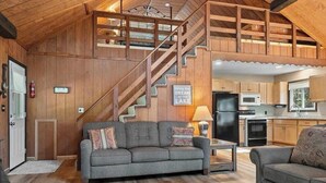 Un intérieur chaleureux avec un escalier en bois, un canapé gris, un coin cuisine et une table à manger.