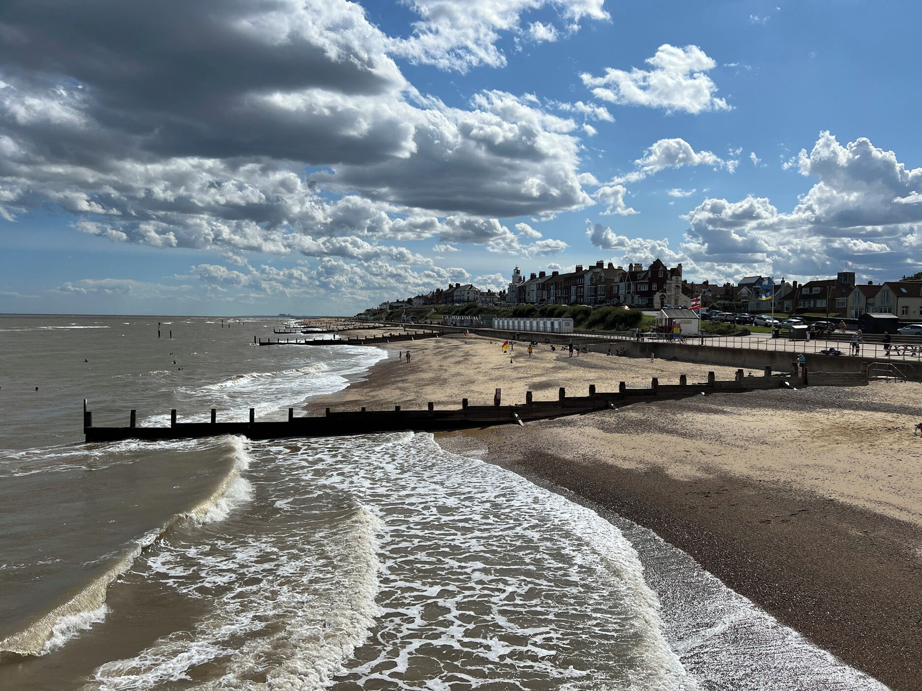 A beach with a promenade, waves, and buildings in the background.