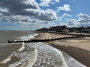 A beach with a promenade, waves, and buildings in the background. - No 1 The Martins (Reydon)