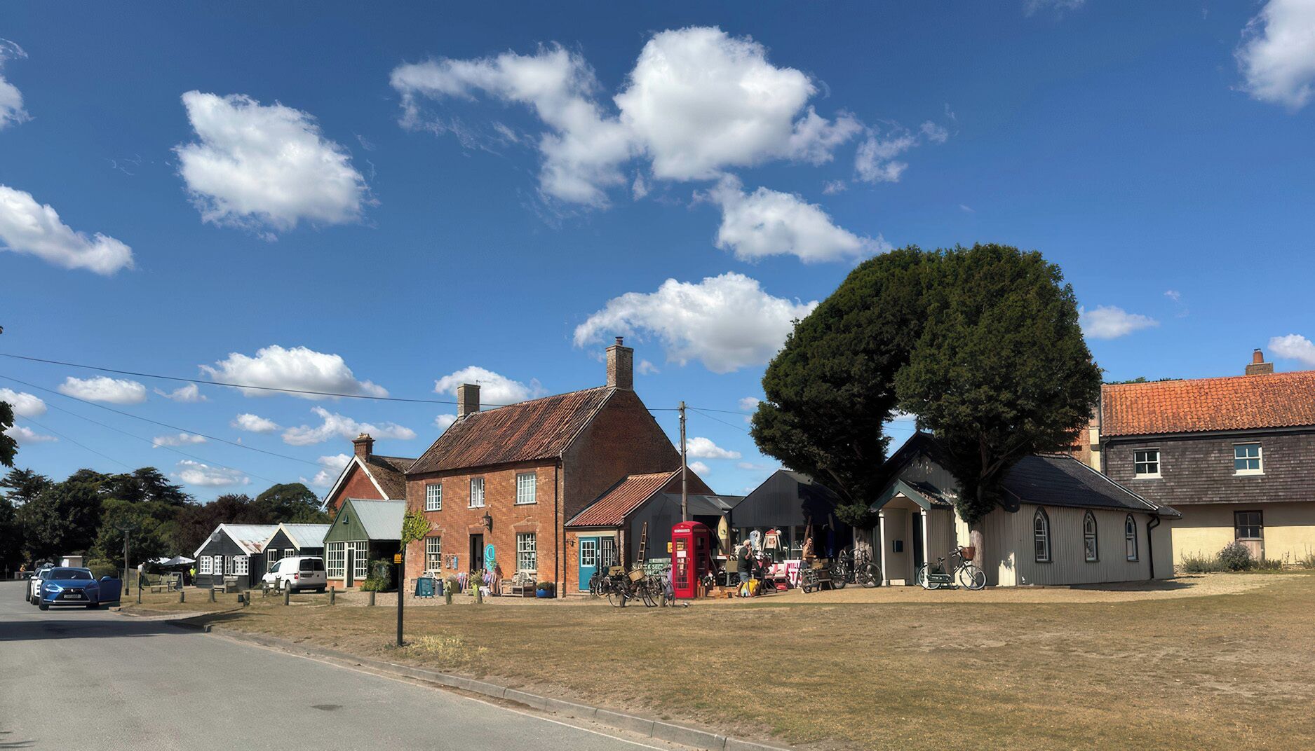 A traditional brick building with a red telephone booth, a large tree, and a clear blue sky.