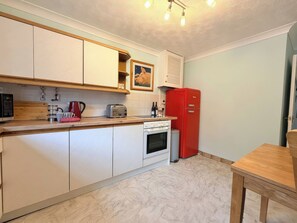 A compact kitchen with white cabinets, a red refrigerator, a wooden countertop, and a small dining table. - No 1 The Martins (Reydon)