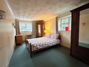 A bedroom with a bed, a wardrobe, a desk, a chair, and a window with curtains. - No 1 The Martins (Reydon)
