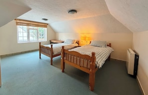 A bedroom with two wooden beds, a window with blinds, a bedside table with lamps, and a radiator. - No 1 The Martins (Reydon)