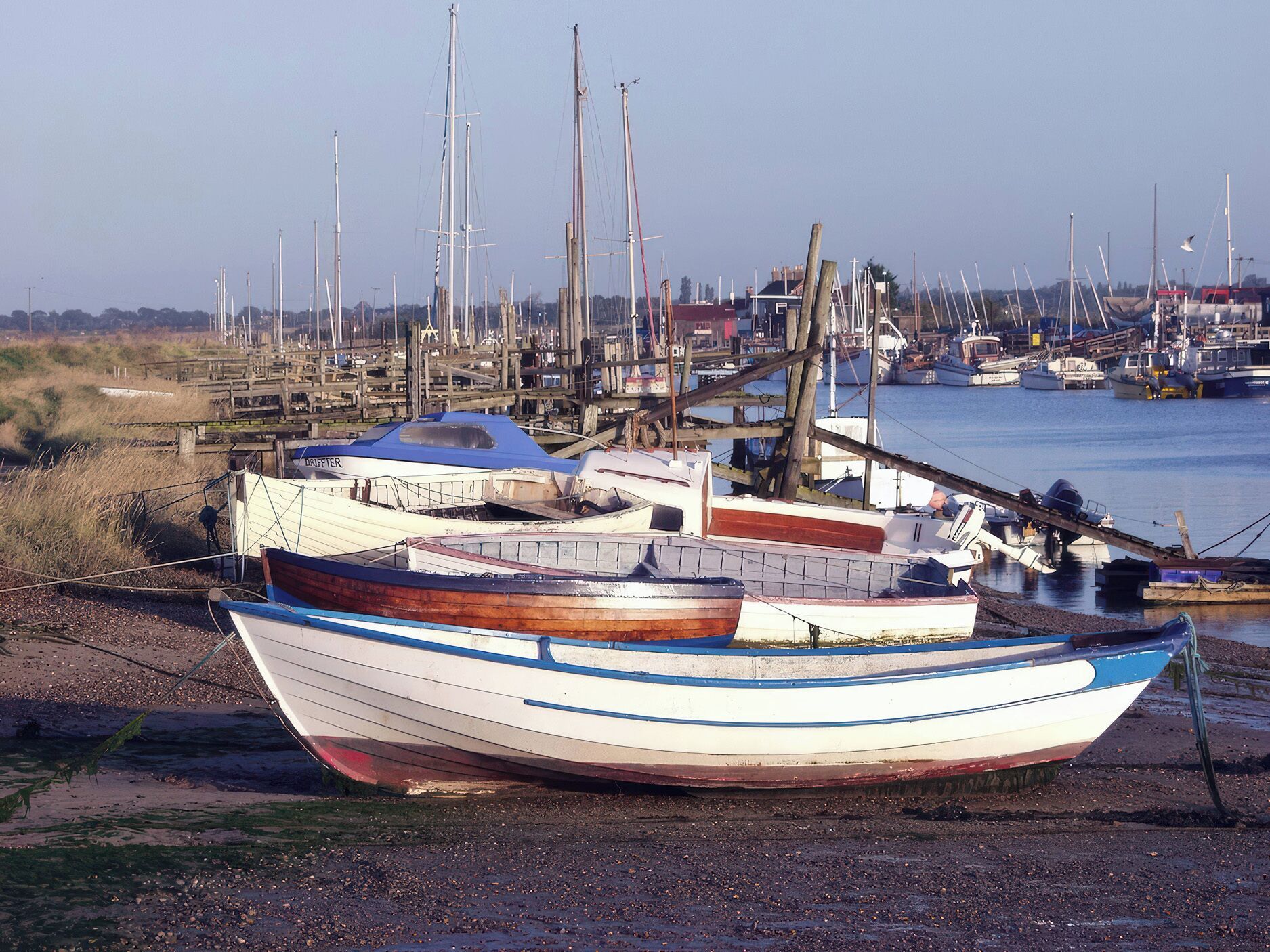 A boat docked at a marina with multiple boats and a wooden structure in the background.