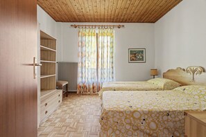 Un dormitori amb dos llits, un armari de fusta, un radiador i una finestra amb cortines.