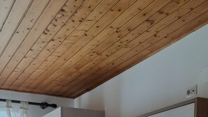 Huoneessa on puinen katto, suuri vaatekaappi, patjallinen sänky ja kuviollinen lattia.